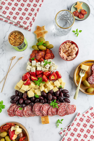 Weihnachts Snackboard in Form eines Tannenbaums mit verschiedenen Sorten Käse, Salami, Oliven und gefüllten Kirschpaprika 