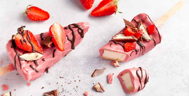 Erdbeere Joghurt Cheesecake am Stiel in einer rosa Schokoladenhülle dekoriert mit Erdbeeren und dunkler Schokolade 
