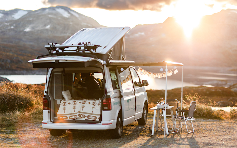 Ausgestatteter Camper mit Überdachung und Tisch an einem See mit Bergpanorama 