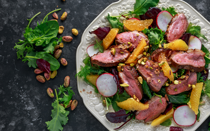 salat-mit-orangen-radieschen-und-entenbrust-auf-einem-weissen-teller-angerichtete