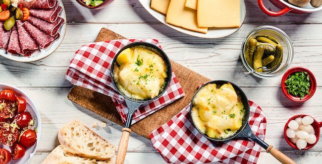 raclette-pfännchen-mit-kartoffeln-und-raclettekäse-auf-einem-holzbrett-mit-roten-servietten